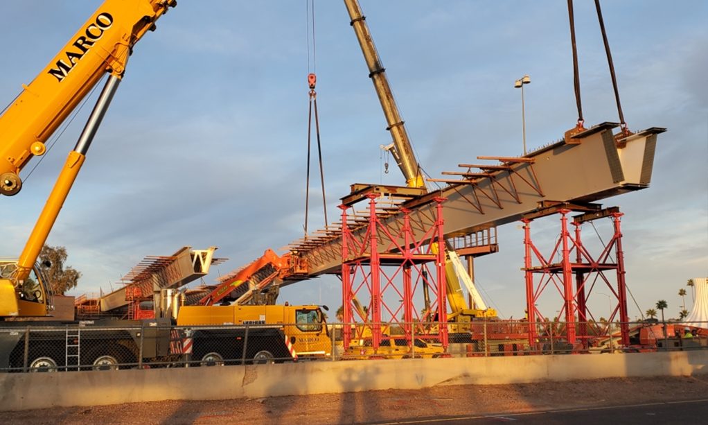 Construction cranes installing large bridge segments at a construction site during sunset, as part of Civil Engineering Services.